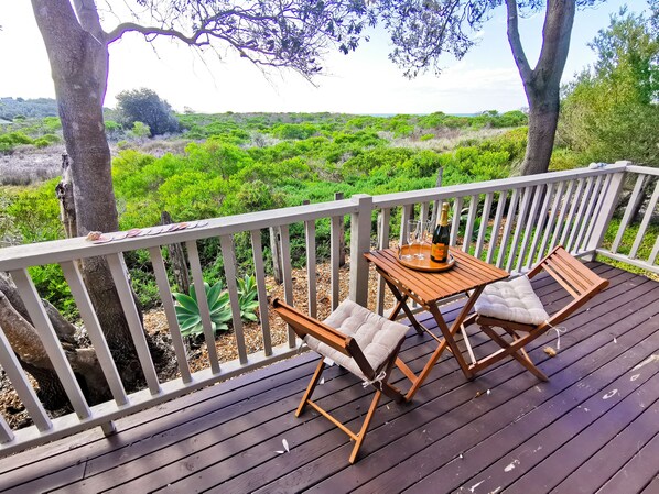 A wooden deck with a table and two chairs, a bottle of champagne, and two glasses on a tray.