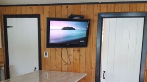 Cuina amb una paret de fusta, un televisor muntat sobre un taulell, un tamboret i un paviment de rajoles.