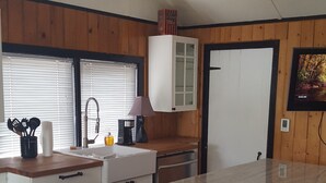 Una cuina moderna amb una illa central, parets de fusta, forn integrat i zona de menjador amb un tamboret.