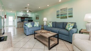 A living room with two sofas, a coffee table, and a lamp. There is a kitchen in the background with a microwave and a refrigerator. - Beachside Escape | Heated Pool, Hot Tub & Ocean Views (Corpus Christi)