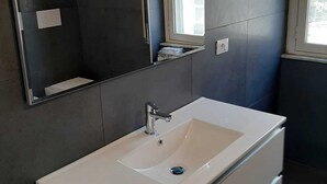 A modern bathroom with a large mirror, a white sink, and a small window. - NEW LUXURY BIG APARTMENT (Pescara)