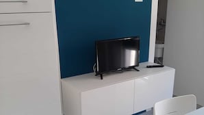 A modern room with a white cabinet, a flat-screen TV, and a white table. - NEW LUXURY BIG APARTMENT (Pescara)