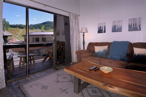 A living room with a brown sofa, a wooden coffee table, and a view through a glass door to an outdoor seating area with a table and chairs. - Emmons Ease, 2BR/2BA,  Remodeled at ski resort, hot tub (Mt. Crested Butte)