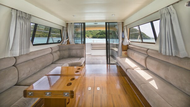 Interior de barco com mesa de jantar central, assentos acolchoados e amplas janelas com vistas panorâmicas.