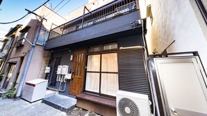 A two-story building with a balcony, a wooden door, and a small air conditioning unit outside.