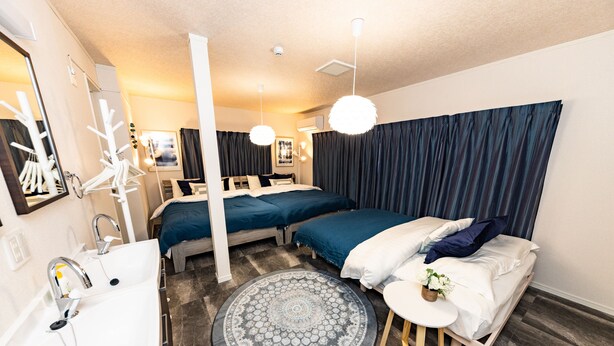 A modern hotel room with a large bed, a separate seating area, a round rug, and a bathroom with a sink and mirror.