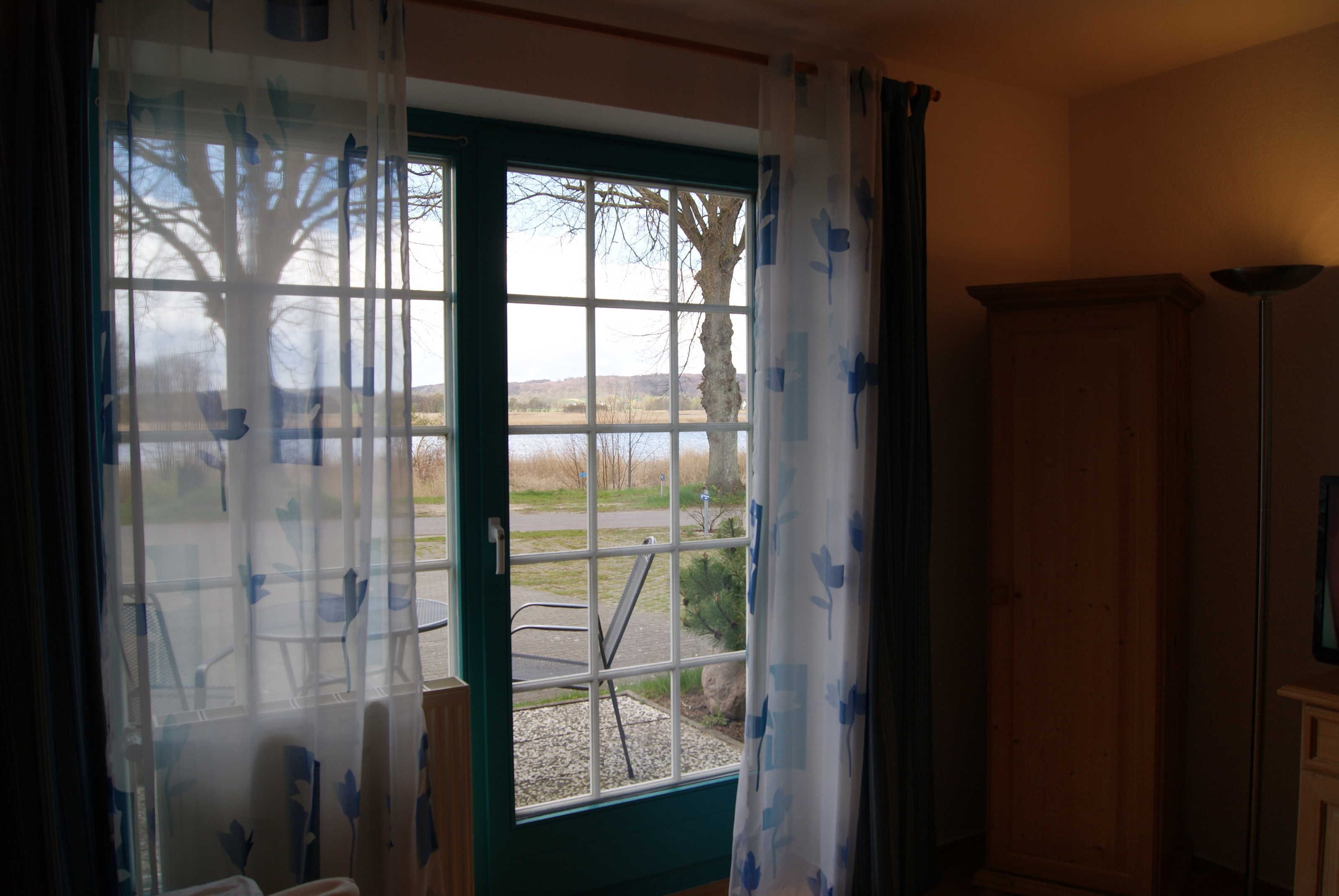 A room with a view through a window, a wooden cabinet, and a chair outside.