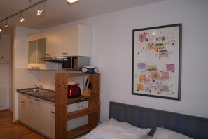 Ein gemütlicher Raum mit Küchenzeile, einem Bett mit Kopfteil und einem Bild in einem Rahmen an der Wand.
