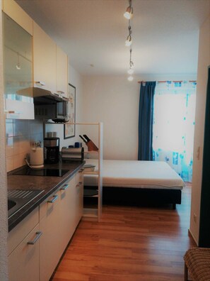 Habitación pequeña con kitchenette, una cama y un ventanal con cortinas.