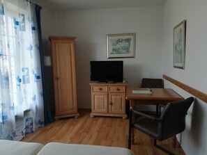Una stanza con un armadio in legno, una televisione, un tavolo, una sedia e un letto.