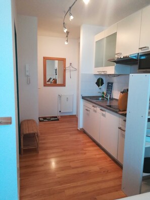 Cocina compacta con armarios blancos, suelo de madera, espejo colgante y horno integrado.