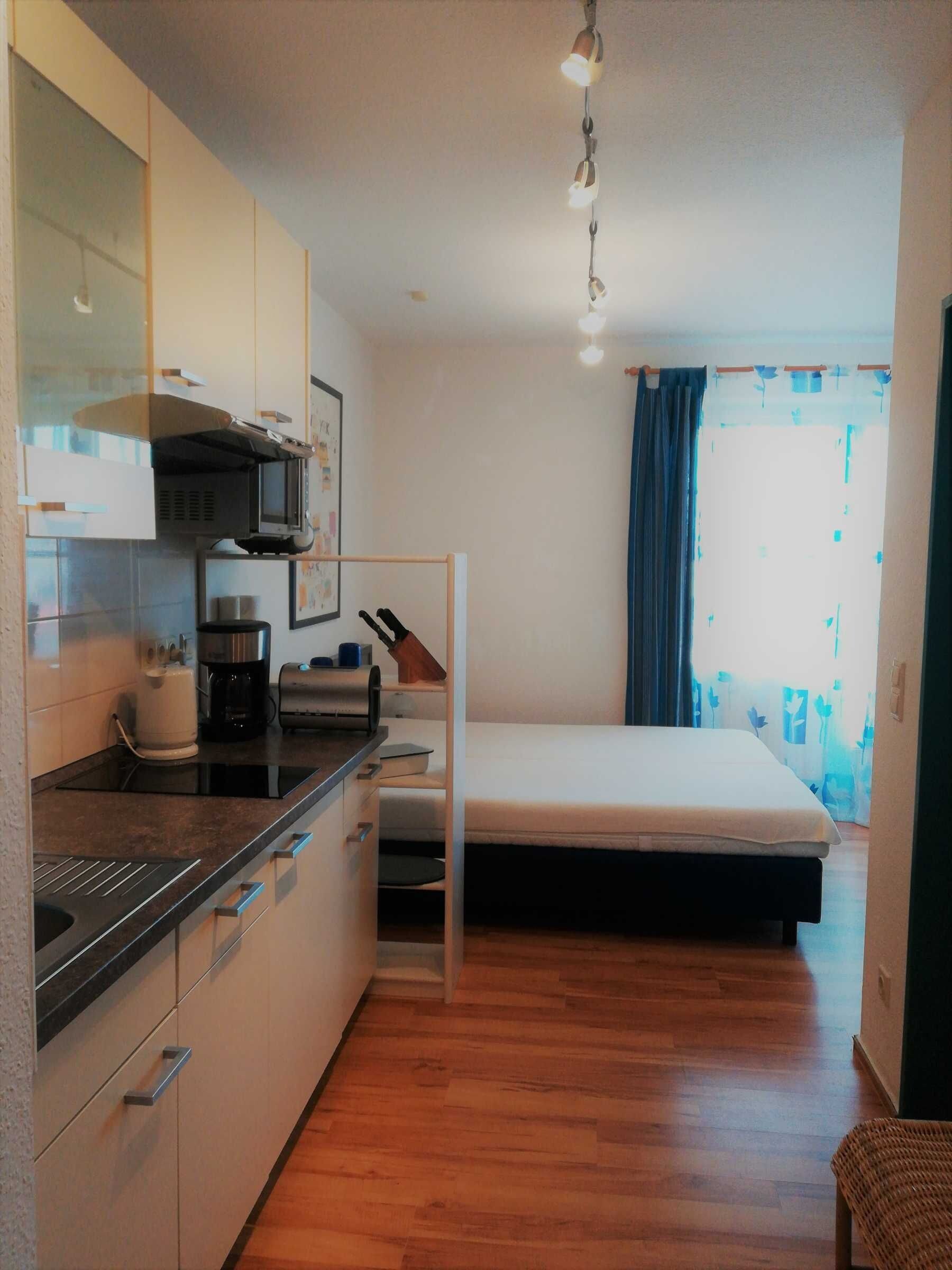 A compact room with a kitchenette, a bed, and a window with curtains.