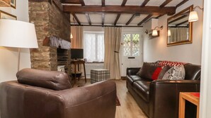 A cozy living room with a stone wall, wooden beams, a leather sofa, a wooden coffee table, and a TV. - Pretty cottage, perfect readers' retreat in centre of Hay, parking & fast wifi (Hay-on-Wye)