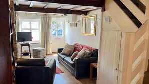 A living room with a sofa, a coffee table, and a television. There is a staircase leading to another level. - Pretty cottage, perfect readers' retreat in centre of Hay, parking & fast wifi (Hay-on-Wye)