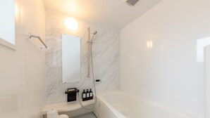 Een moderne badkamer met een witte badkuip, een handdouche, een wandspiegel en een zeepdispenser op een wit aanrecht.