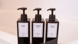 Drie flessen shampoo, conditioner en douchezeep op een witte wasbak.