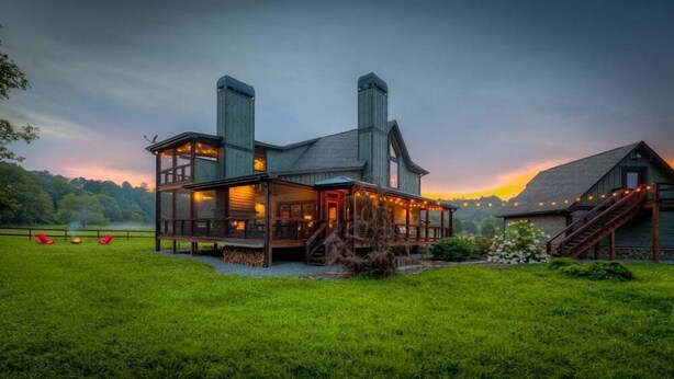 A large, multi-story wooden house with a prominent chimney, a covered porch, and a well-maintained lawn. - Firefly Farmhouse - Riverfront | Modern | 2 Bedroom w loft (Blue Ridge)