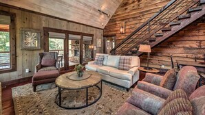 A rustic cabin interior with a wooden staircase, a sofa, armchairs, and a round coffee table. - Firefly Farmhouse - Riverfront | Modern | 2 Bedroom w loft (Blue Ridge)