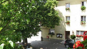 Un espace extérieur aménagé avec des tables et des chaises, un bâtiment orné de jardinières et une voiture garée.