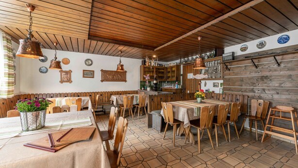 Un coin repas rustique avec des tables et des chaises en bois, une cuisine en arrière-plan et un sol carrelé.