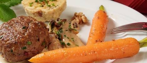 A plate with a meat patty, a carrot, and a small mound of food, possibly a side dish.