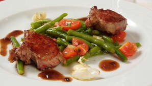Une assiette contenant un steak, des haricots verts et des tomates.