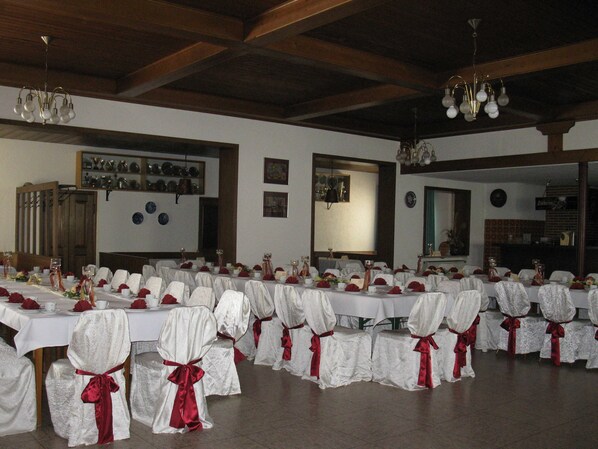 Une salle de banquet où les tables sont dressées pour un événement officiel, avec des nappes blanches et des rubans rouges sur les chaises.
