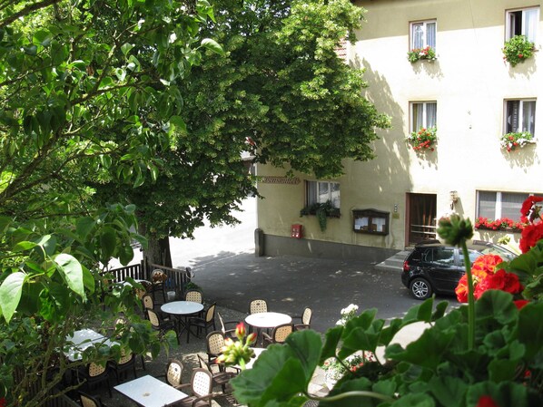 An outdoor seating area with tables and chairs, a building with flower boxes, and a parked car.
