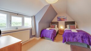 A bedroom with two beds, a desk, a radiator, and a window with a view.