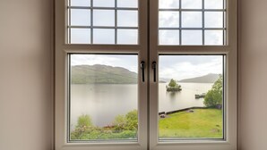 A window with a view of a lake, mountains, and a grassy area.