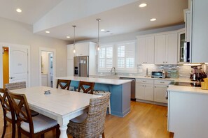Una cocina moderna con armarios blancos, una isla central y un comedor con sillas de madera.