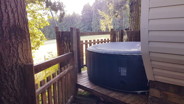 Un bain à remous sur une terrasse en bois, avec une clôture en bois et des arbres en arrière-plan.