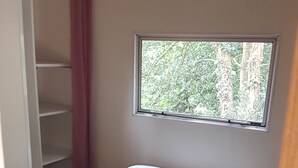 Une chambre à coucher avec un lit, une fenêtre donnant sur des arbres, une armoire et une porte.