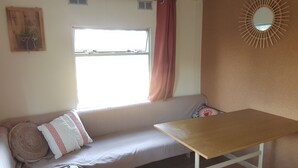 Une pièce comprenant un canapé, une table, une fenêtre avec des rideaux, un miroir fixé au mur et une petite plante.