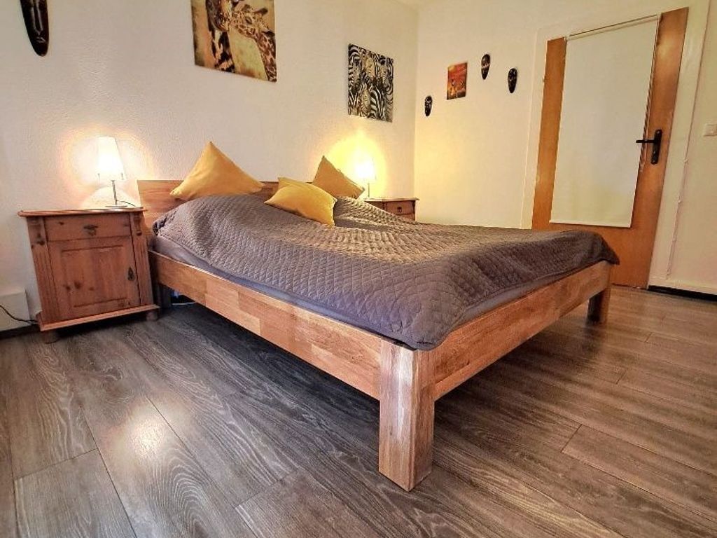 Ein Bett mit Holzbettgestell und Patchworkdecke, zwei Nachttische mit Lampen sowie eine Tür in einem Zimmer mit Holzboden.