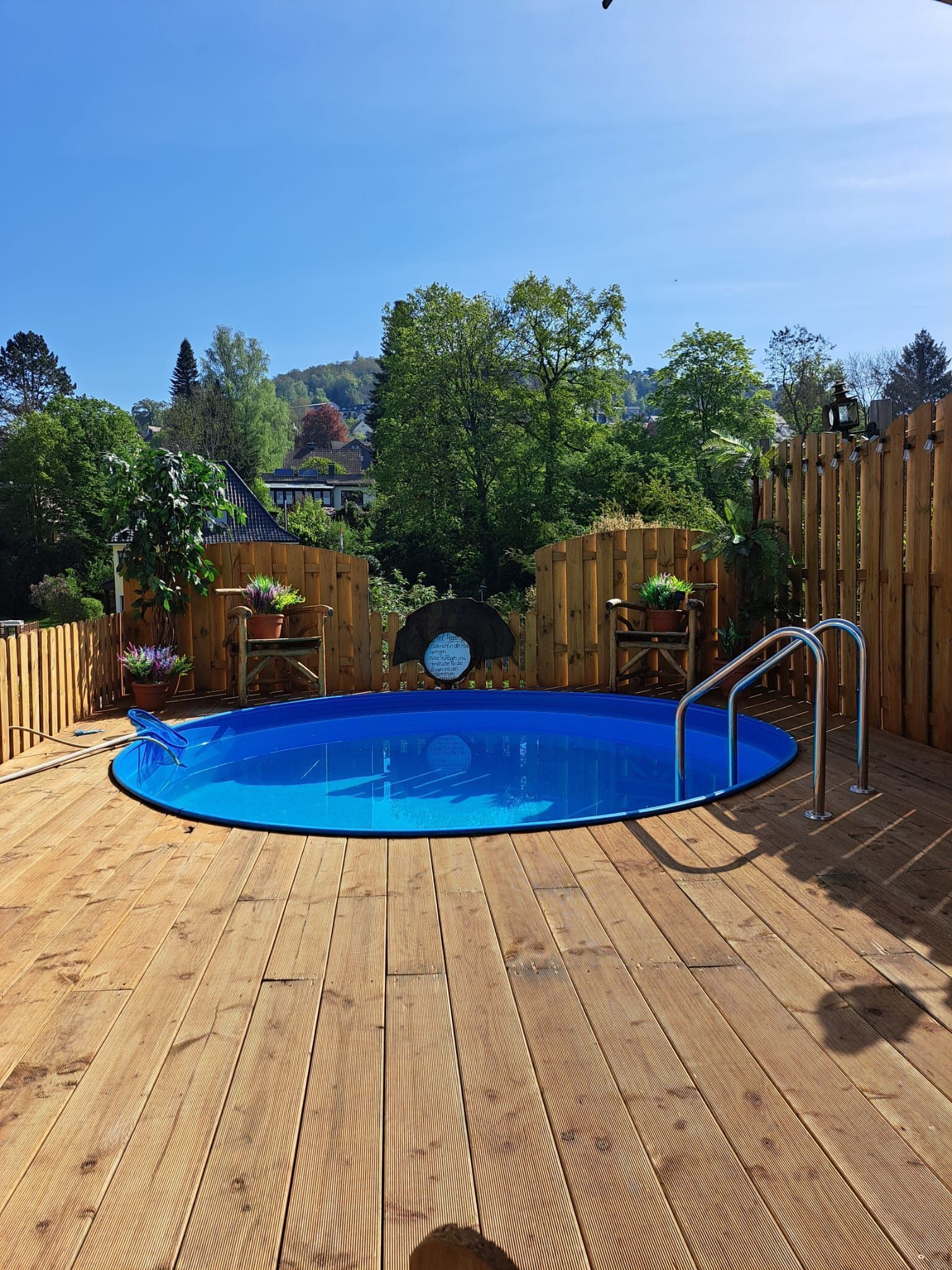 Eine Holzterrasse mit einem blauen Pool, umgeben von Holzzauns und Kübelpflanzen.