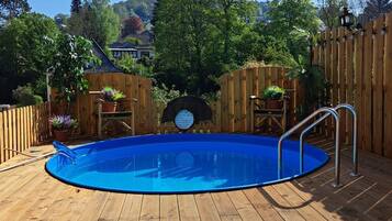 Eine Holzterrasse mit einem blauen Pool, umgeben von Holzzauns und Kübelpflanzen.