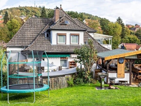 A house with a sloped roof, a trampoline, and a covered outdoor area with a table and chairs.