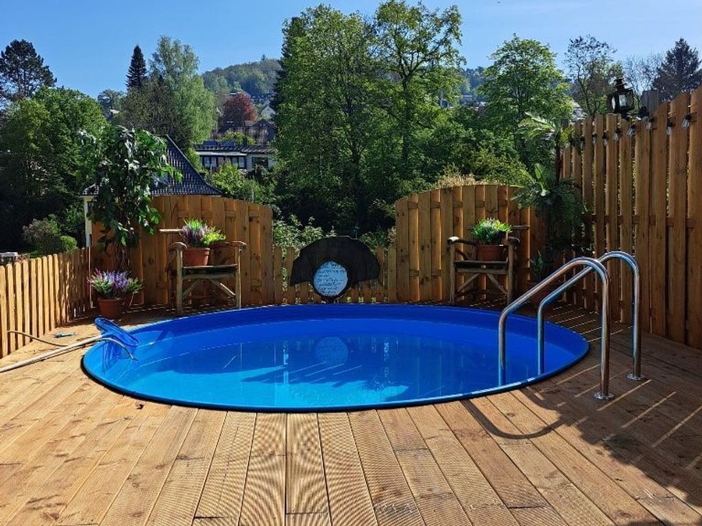 Eine Holzterrasse mit einem blauen Pool, umgeben von Holzzäunen und Topfpflanzen.