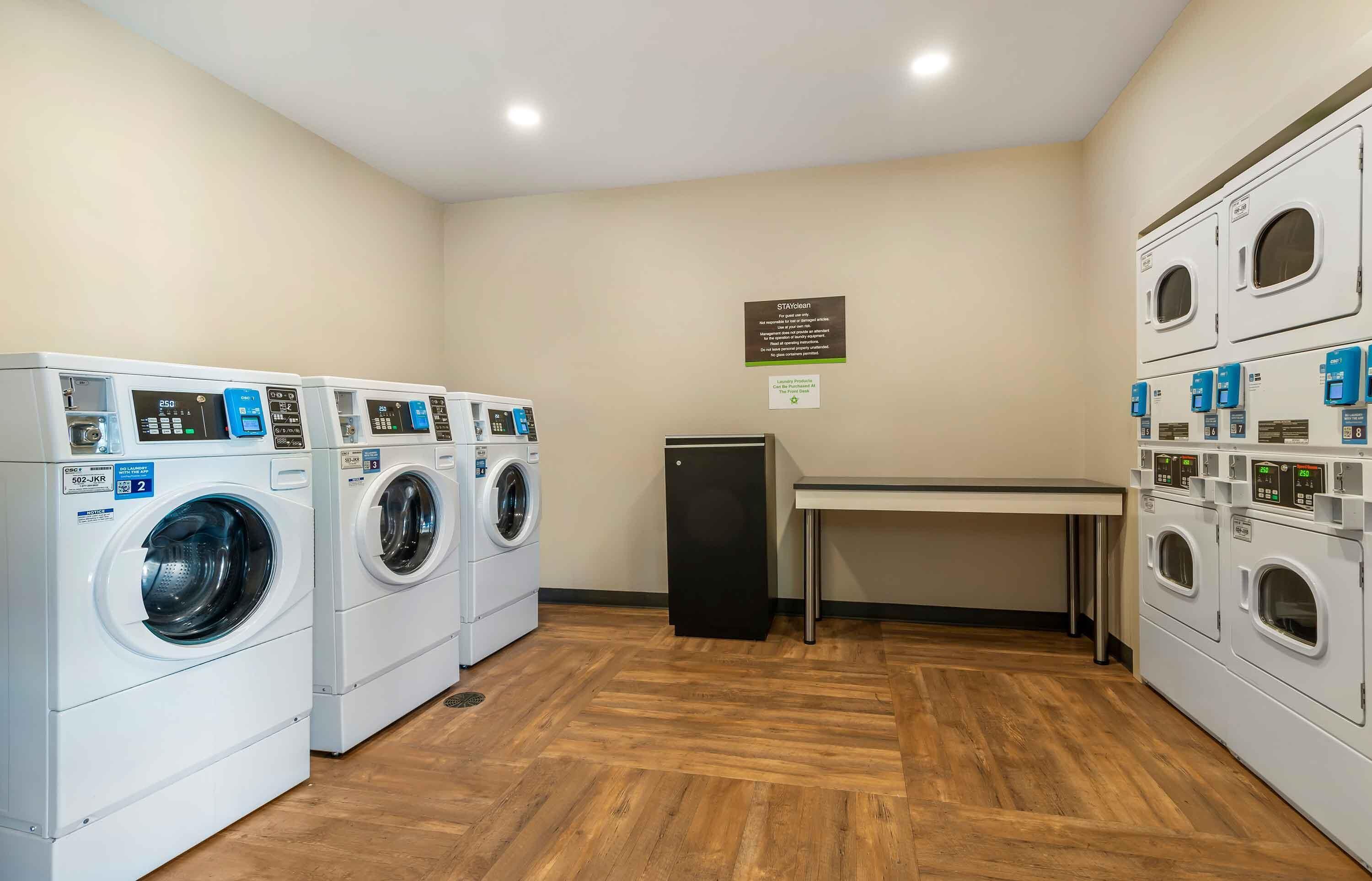 A laundry room with multiple washing machines, a table, and a refrigerator.