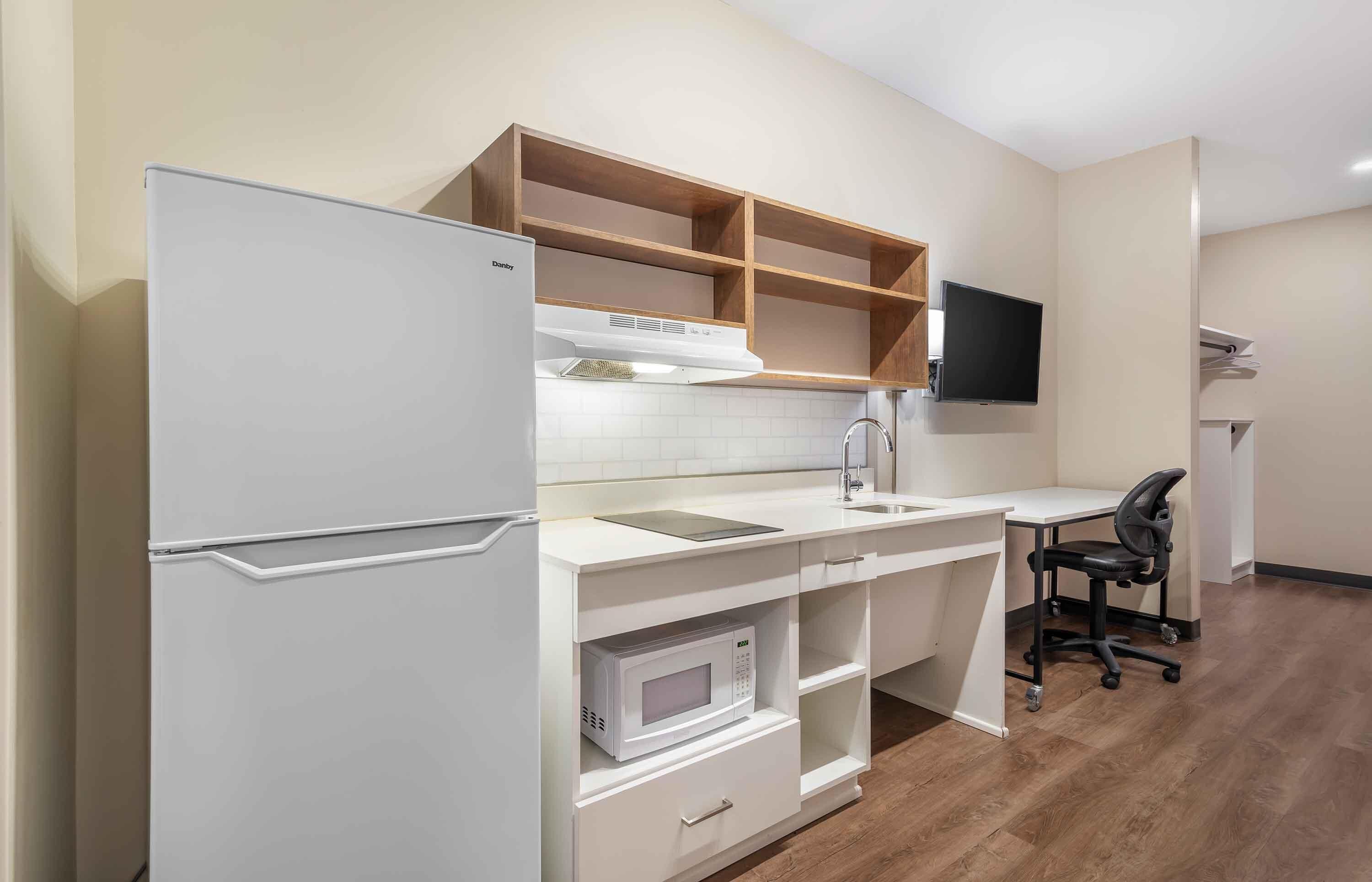 A compact kitchen with a refrigerator, microwave, and wooden shelves above the counter.