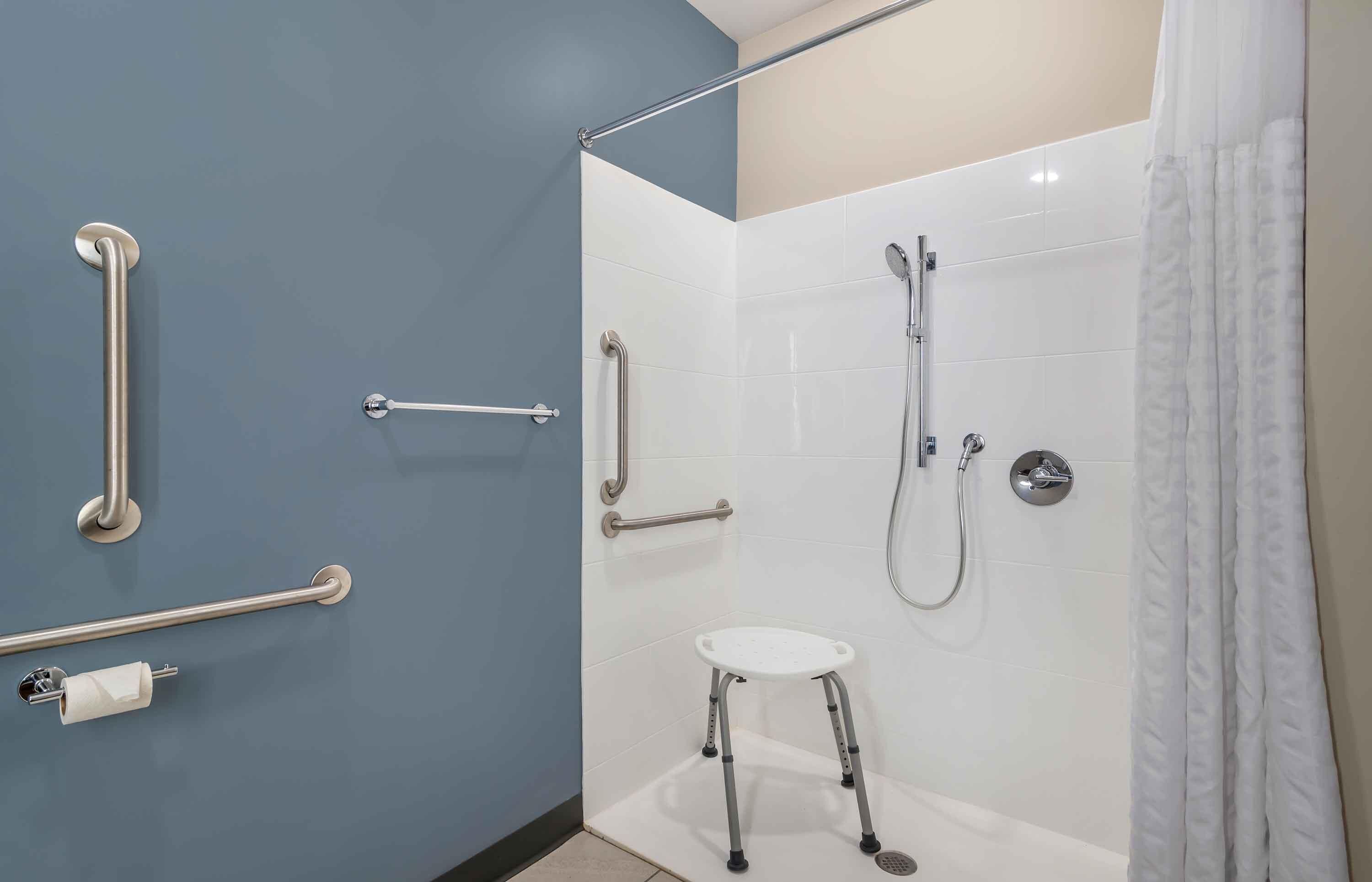 A bathroom with a shower, grab bars, a toilet, and a step stool.