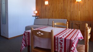 Una habitación con pared de madera, un sofá, una mesa con mantel estampado y dos lámparas fijadas a la pared.