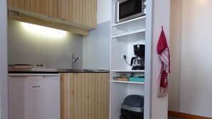 Cocina compacta con armarios de madera, microondas, cafetera y un cubo de basura.