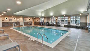 A large indoor swimming pool with clear lane markings, a lifeguard chair, and a seating area with tables and chairs.