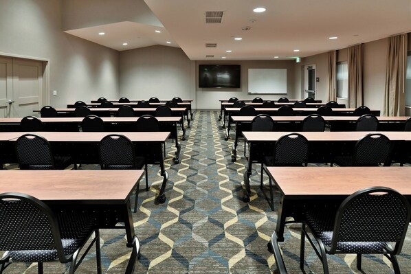 A conference room with rows of tables and chairs, a large screen, and a patterned carpet.