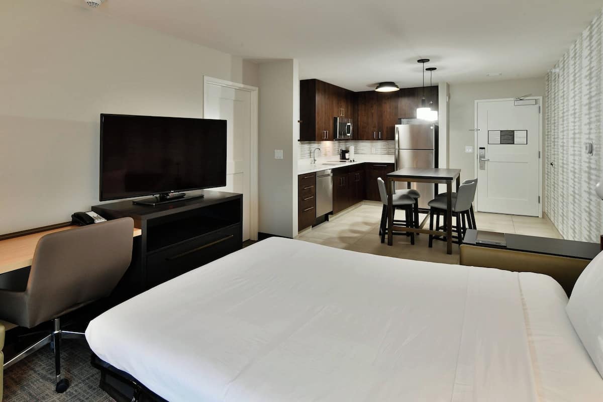 Une chambre d’hôtel comprenant un lit, un bureau avec une chaise, une télévision, une kitchenette et une salle de bain.