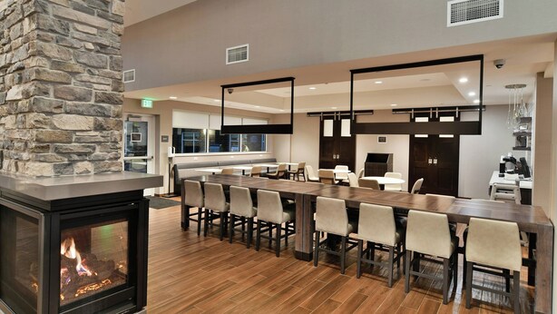 A modern interior with a stone fireplace, a long dining table with chairs, and a kitchen area in the background.