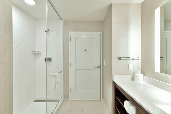 A modern bathroom with a glass shower enclosure, a white door, and a large mirror above a white sink with a towel rack.