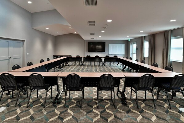 A conference room with a long table, black chairs, a patterned carpet, and a large screen on the wall. - Residence Inn by Marriott Eau Claire (Eau Claire)